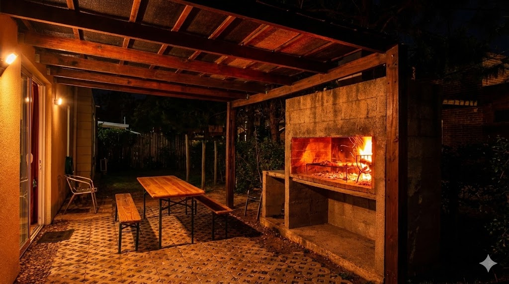 Parrillero encendido de noche junto a una mesa bajo la galería